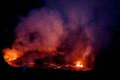 Vibrant colors, reds, pinks and yellows surround crater of active volcano glowing in the nighttime sky Stock Photo